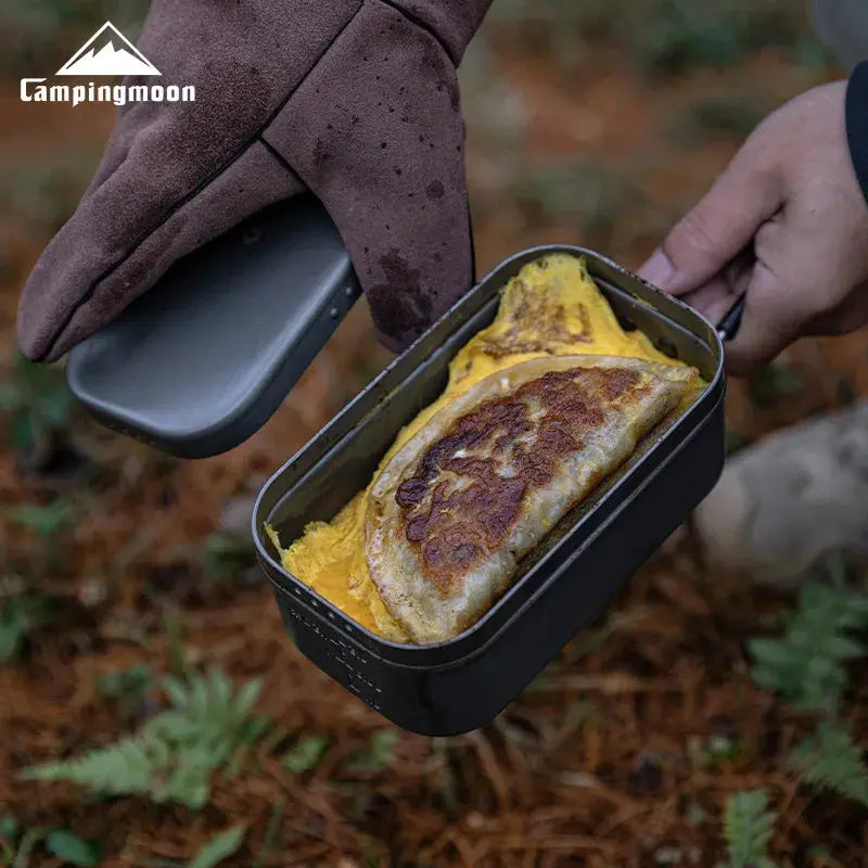 CampingMoon aluminum portable lunch box, black metal open-flame camping lunch container with food inside.