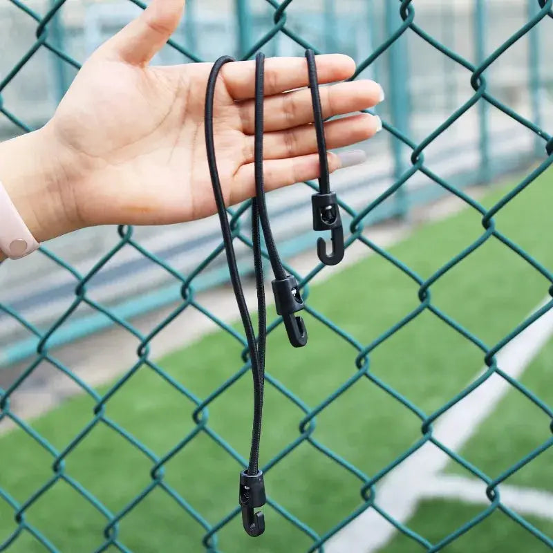 Bungee cords with hooks, black elastic cords held by hand beside a chain-link fence