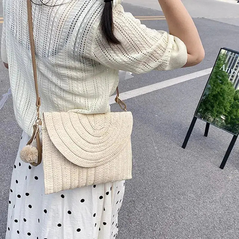 Handmade beige straw crossbody bag by Simples Market with envelope flap and pom-pom charm