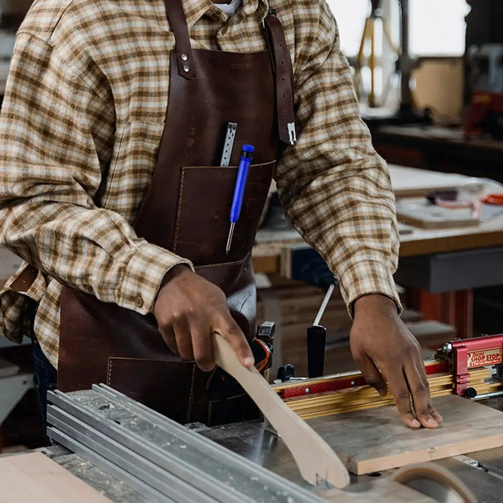 Top Solid carpenter mechanical pencil in blue, tucked in a leather apron pocket of a woodworker at a workbench