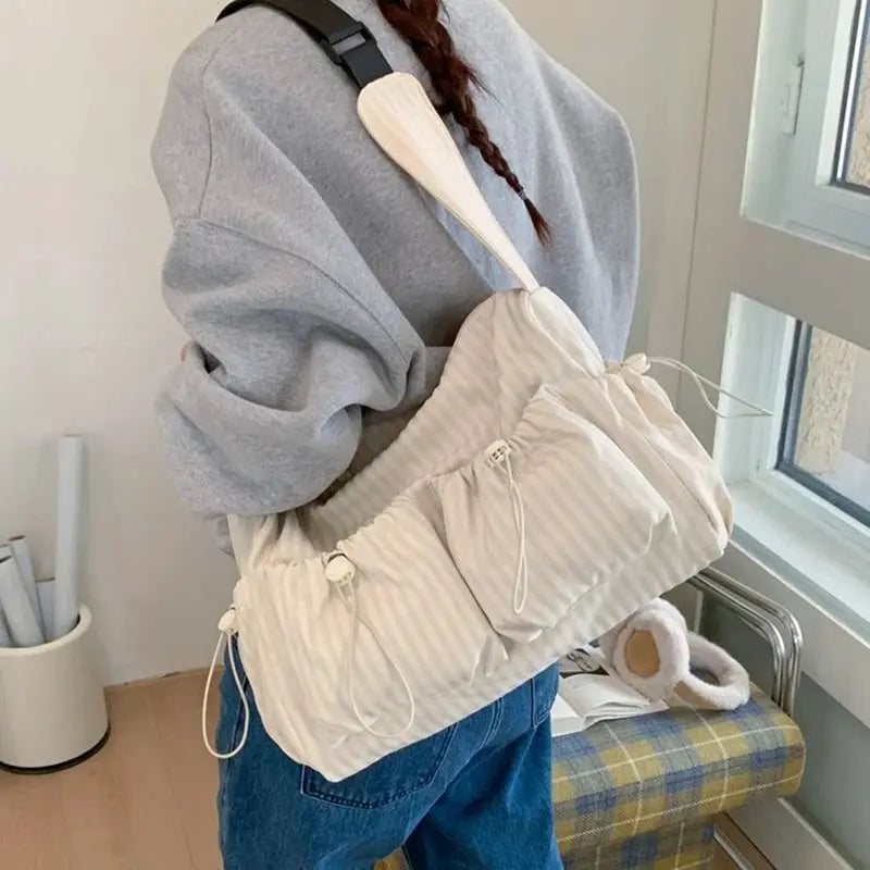 Korean nylon shoulder bag in cream striped fabric with drawstring closure and zip pockets, worn crossbody