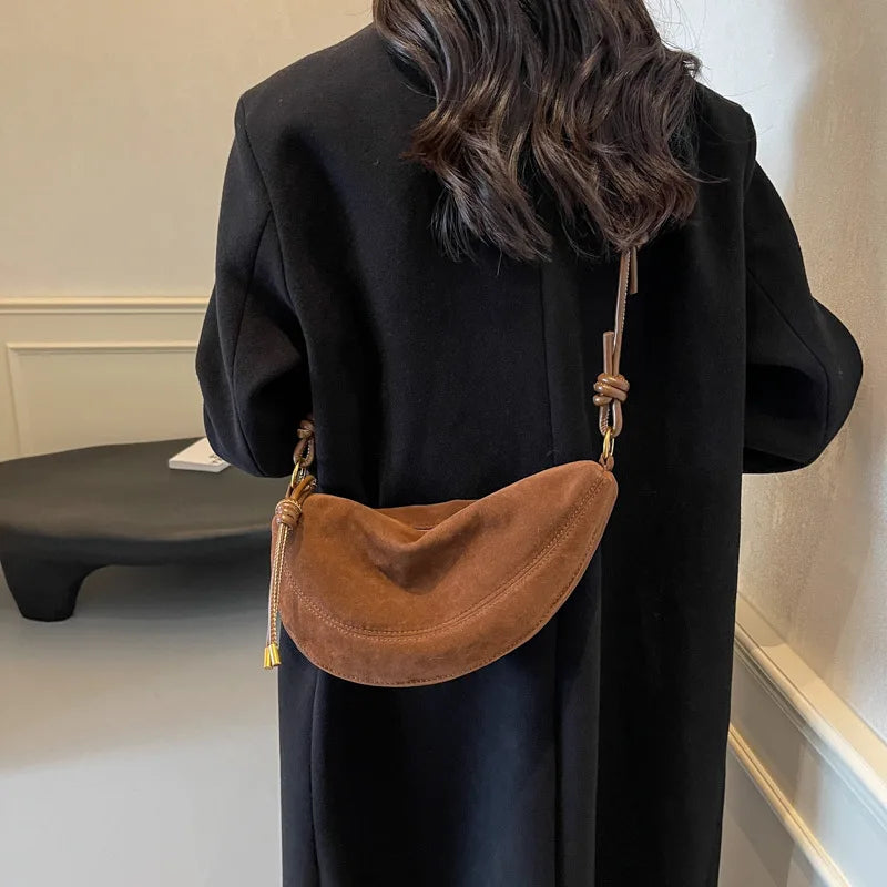 Faux suede dumpling shoulder bag, tan brown crossbody worn by a woman in a black coat.