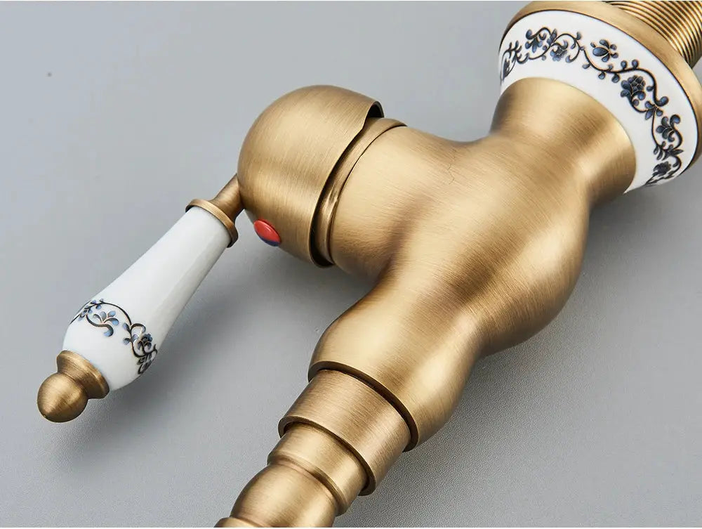 Antique brass bathroom faucet with rotating spout and white porcelain handle with blue floral pattern