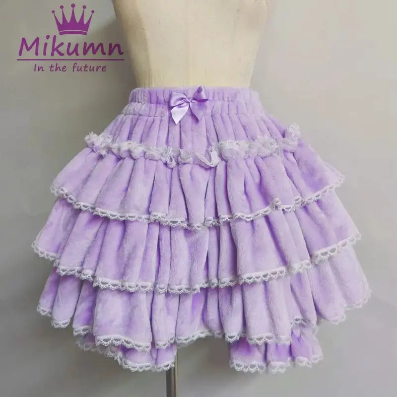 Lavender Lolita-style layered skirt with ruffles, white lace trim, and a bow at the waistband, Mikumm watermark