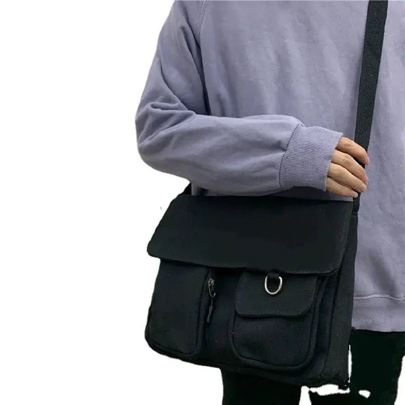 Women's black canvas messenger bag with front zip pocket, D-ring accent, and crossbody strap.