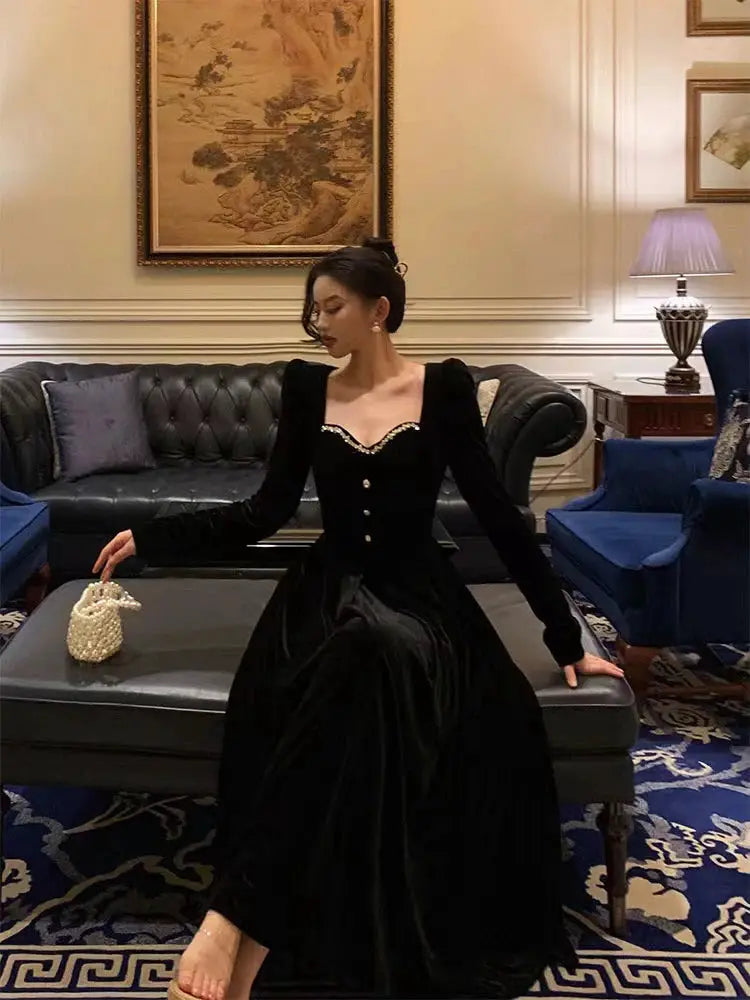 Gidyq fashion women's black velvet dress with pearl-trimmed sweetheart neckline and long sleeves, model seated on sofa