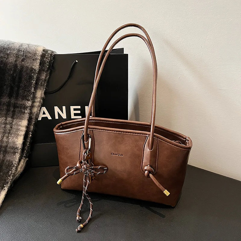 Brown PU leather shoulder bag with double top handles and tassel charm; Chanel shopping bag in background
