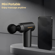 Mini portable massage gun, black handheld deep-tissue massager with ergonomic grip beside a smartphone