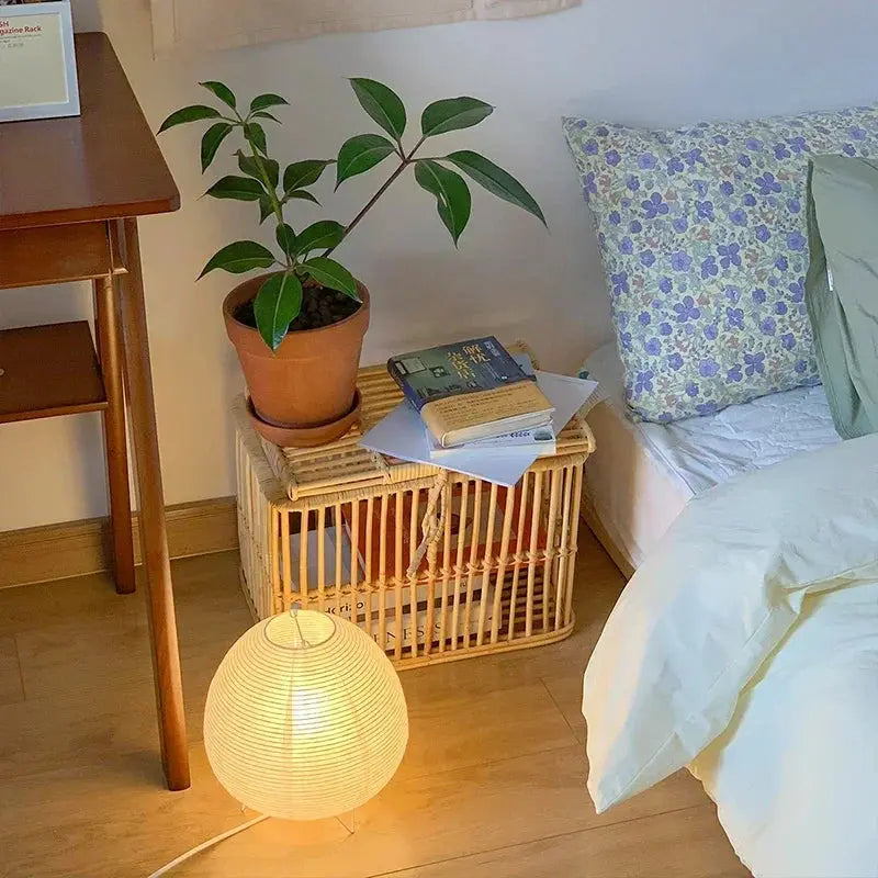 Japanese lantern LED table lamp with white rice paper shade, warm glow beside bed on a wicker nightstand