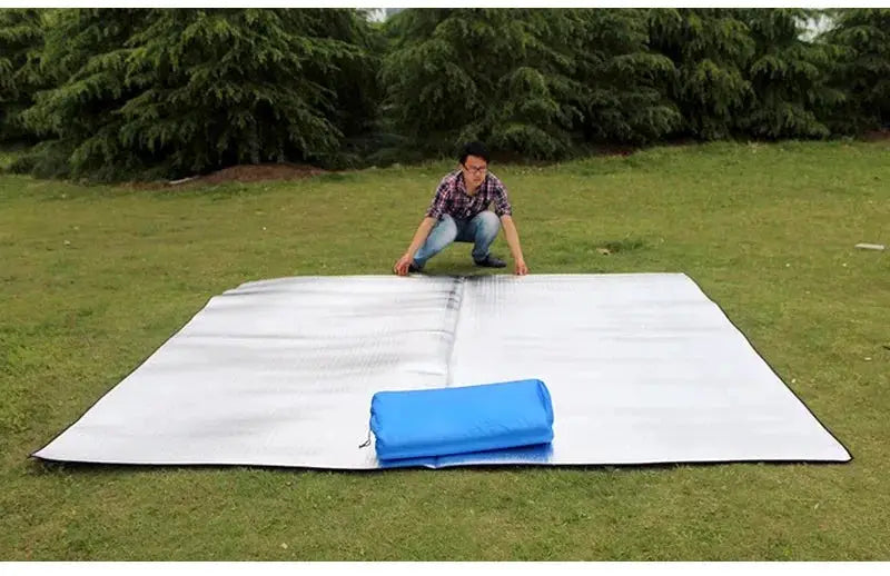 Camping mat with aluminum insulation and reflective foil on grass, blue rolled bag beside