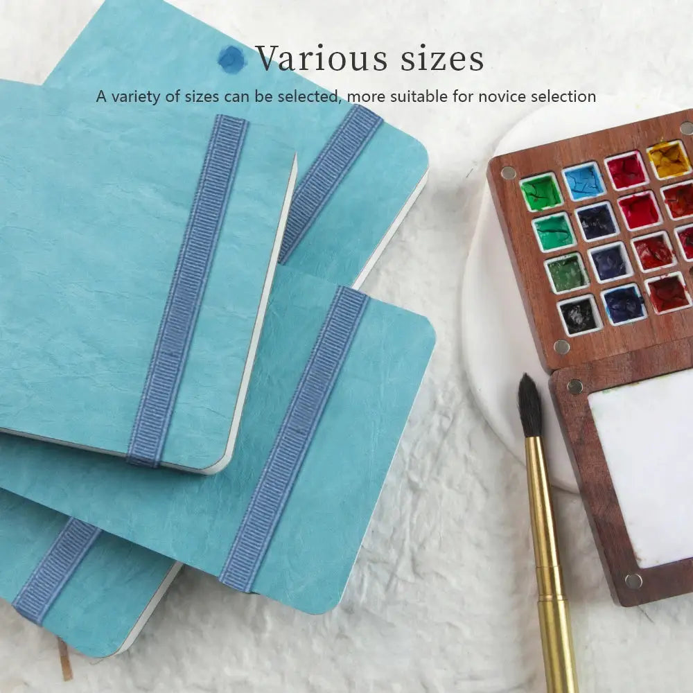 Three Potentate blue watercolor journals with elastic bands in various sizes, paired with a watercolor palette and brush
