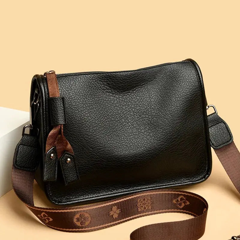 Genuine black leather crossbody bag with brown adjustable strap and tassel zipper pulls.