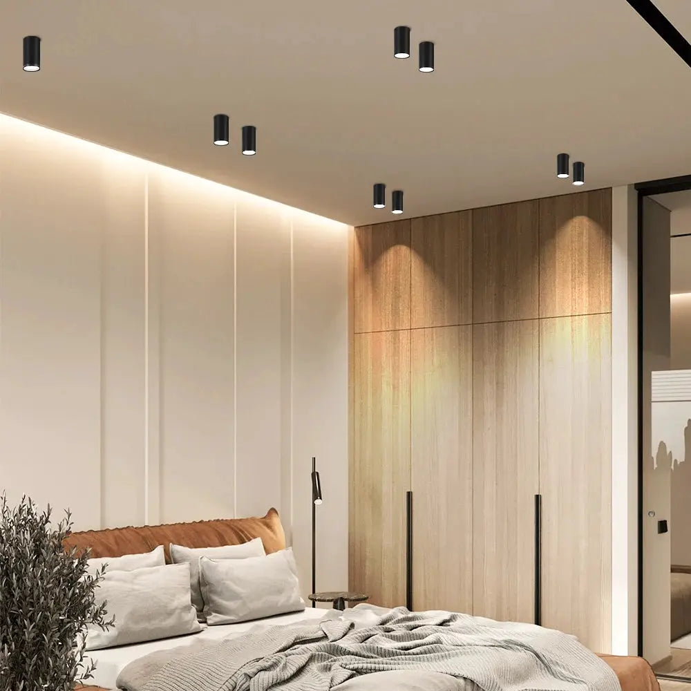 Replaceable bulb GU10 ceiling downlights, nine black cylindrical LED spotlights by Simples Market in a modern bedroom.