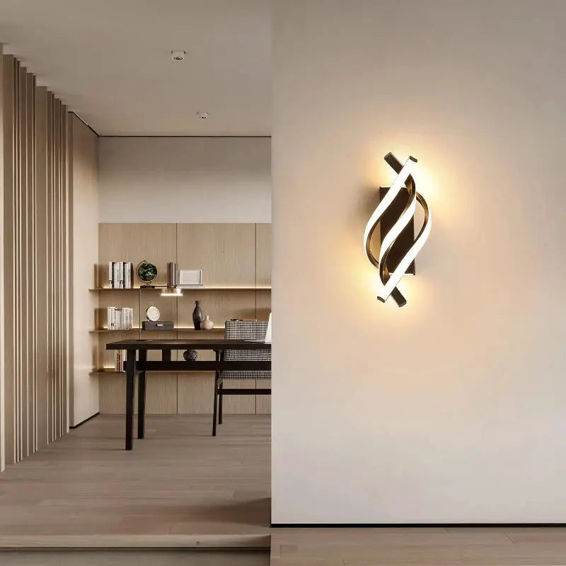 Curved spiral LED wall lamp with metal ribbons and warm white glow on a white wall.