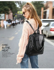 Black soft leather backpack with multiple zipper pockets, worn by a woman on a city street