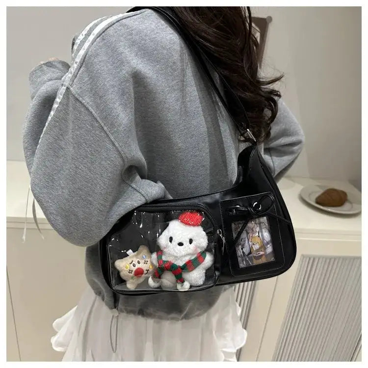 Ita bag, black with transparent panels, holding two plush toys, worn crossbody by a person in a gray hoodie.
