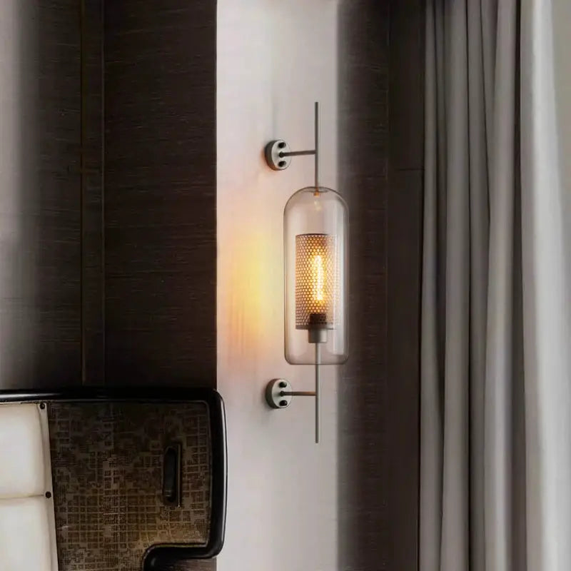 Modern glass wall sconce with clear cylindrical shade and warm golden filament bulb