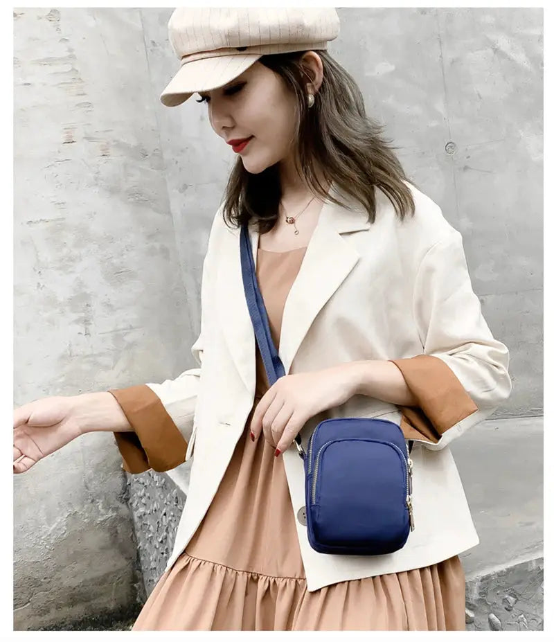 Blue crossbody bag by Simples Market with zip pocket, worn by a woman in beige outfit.