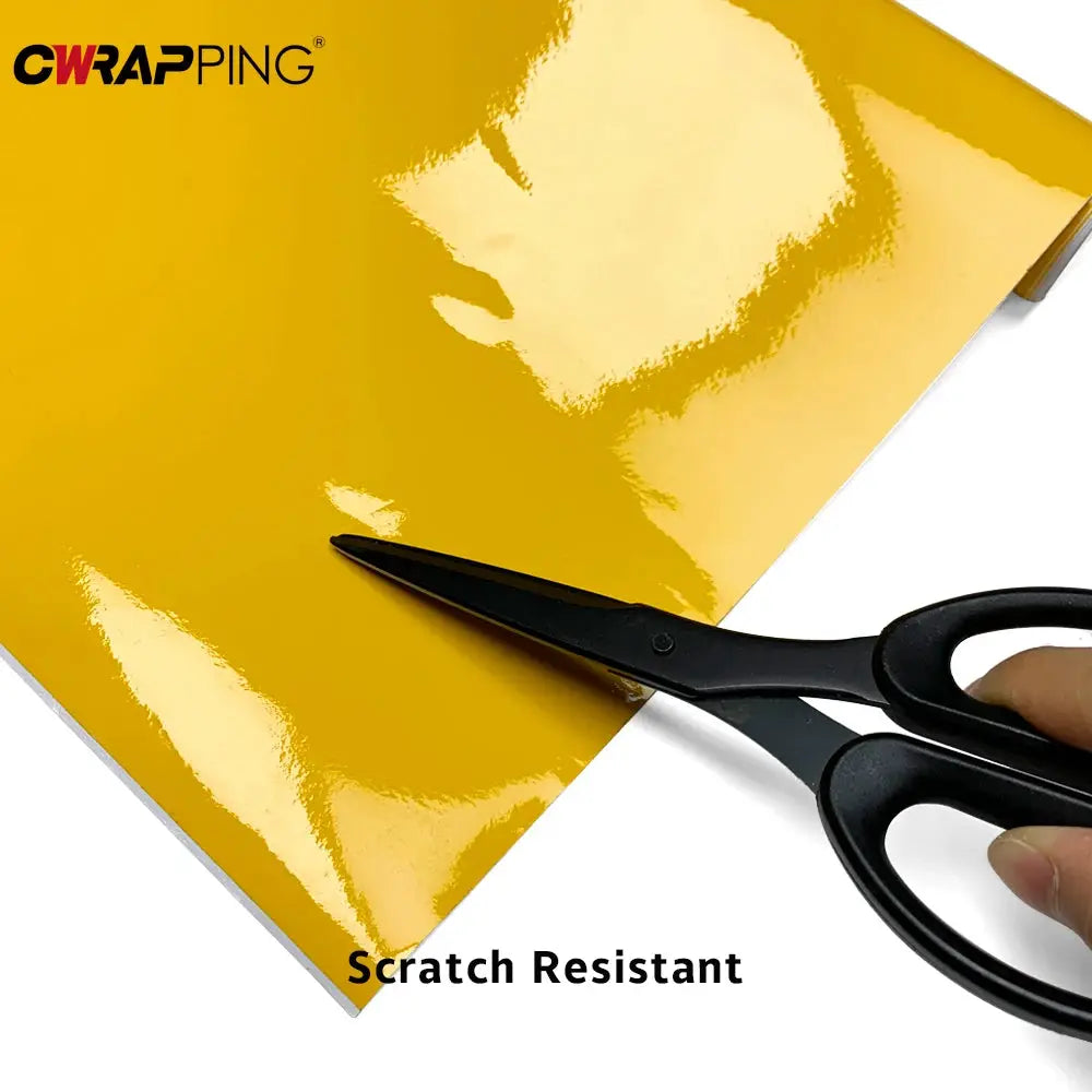 Glossy yellow vinyl wrap sheet with CWRAP PING logo, being cut with scissors; scratch-resistant film