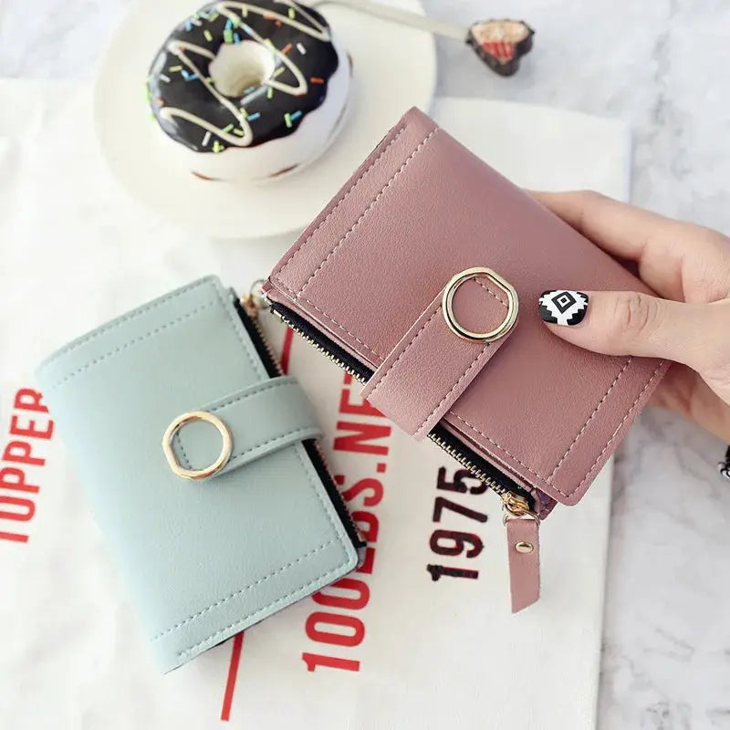 Two women's PU leather zipper wallets in pink and light blue with ring strap details.