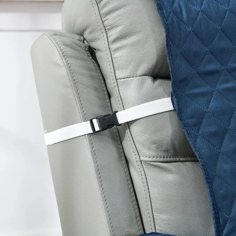 Anti-slip recliner chair cover in blue quilted fabric with a white strap on a gray leather armchair.