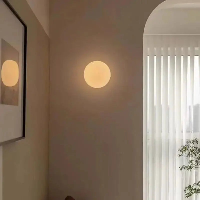 Milky white glass ball wall lamp by Simples Market; frosted round wall light with warm glow.