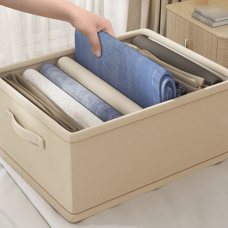 Clothes organizer storage box in beige fabric with handles, filled with folded garments