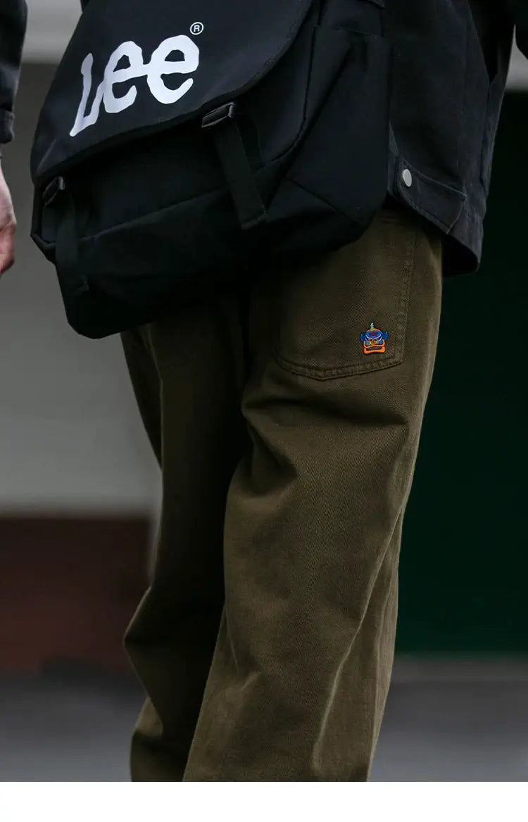 Cargo pants for men in olive with cargo pockets and a small embroidered patch on the thigh; Lee backpack visible.