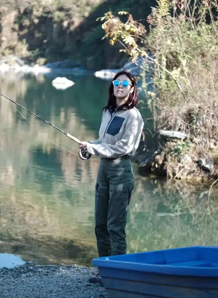 Unisex fleece sweatshirt with a semi-zip, gray fabric and dark chest pocket, worn by a woman fishing beside a lake