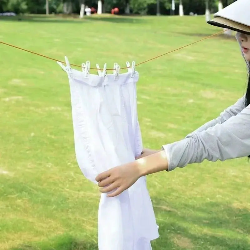 Retractable outdoor clothesline rope with windproof anti-slip clips; white laundry hanging in a park.