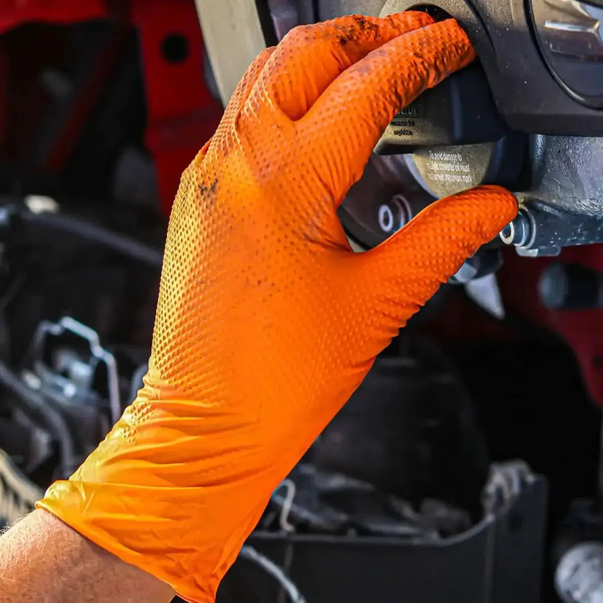 Heavy-duty nitrile glove, orange with textured grip, worn while working on machinery.