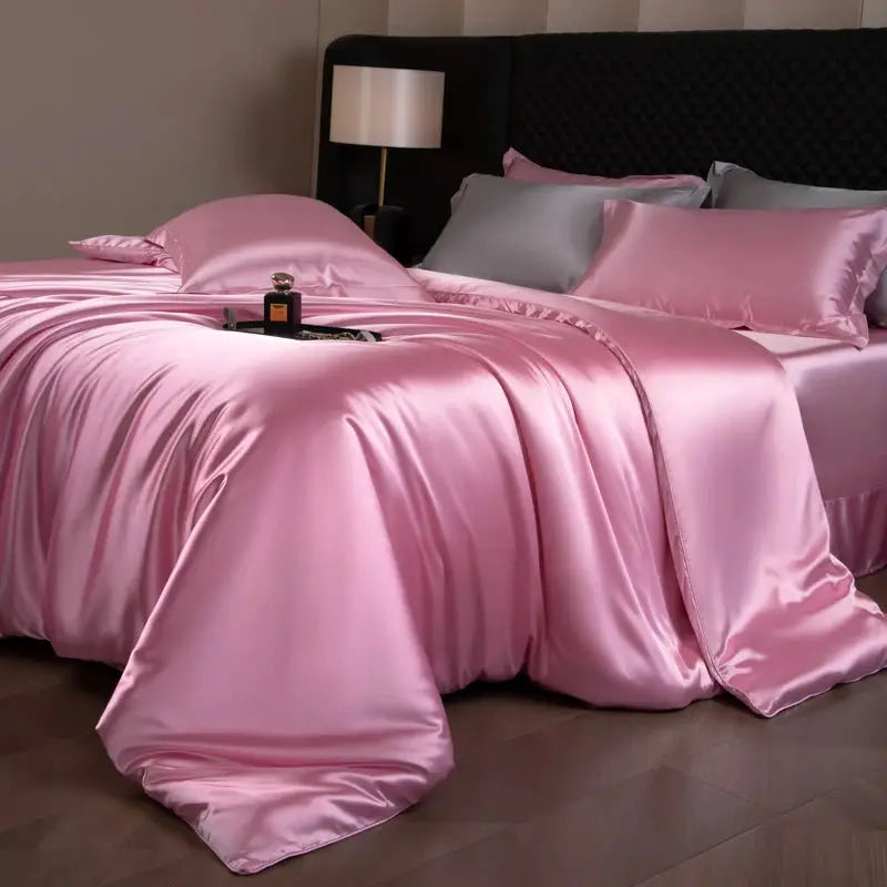 Pink silk bedding set with duvet cover, fitted and flat sheets, and pillowcases on a bed