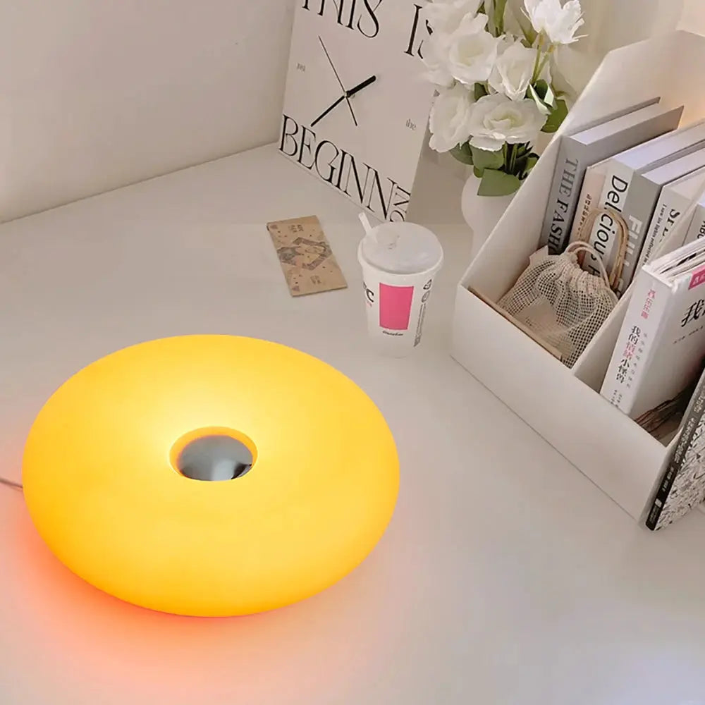 Bauhaus donut table lamp with warm amber glow and plastic body on a white desk