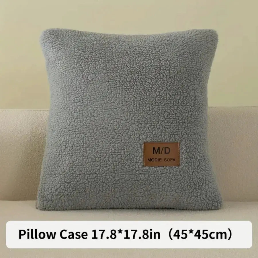 Pillow with grey sherpa fabric and brown M/D MODE SOFA label patch, square 17.8x17.8 in (45x45 cm).