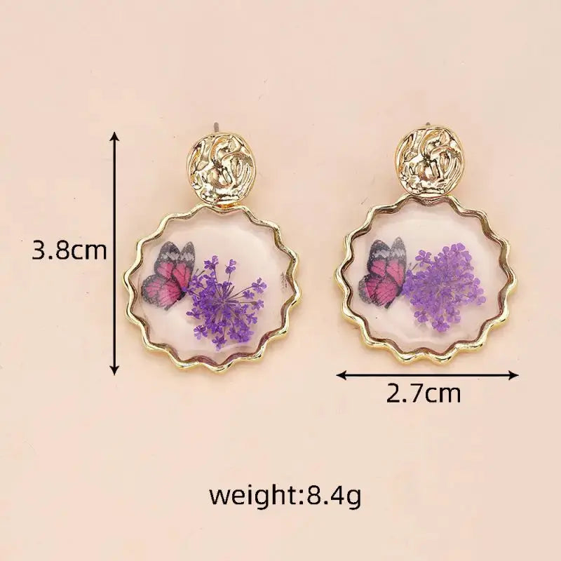 Pair of gold-tone epoxy resin dangle earrings with scalloped circular frames containing purple pressed flowers