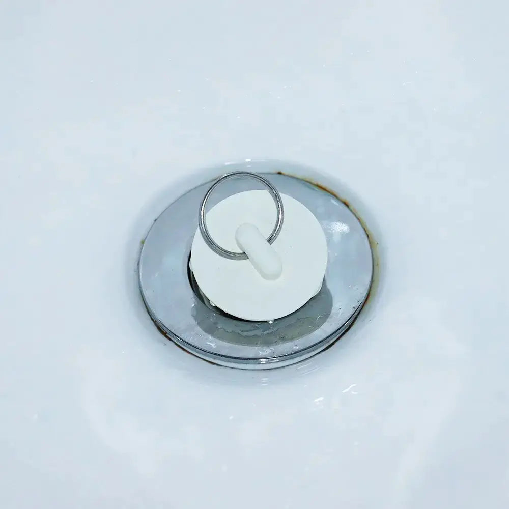 Rubber sink drain plug with white circular stopper and metal ring for bathroom and laundry.