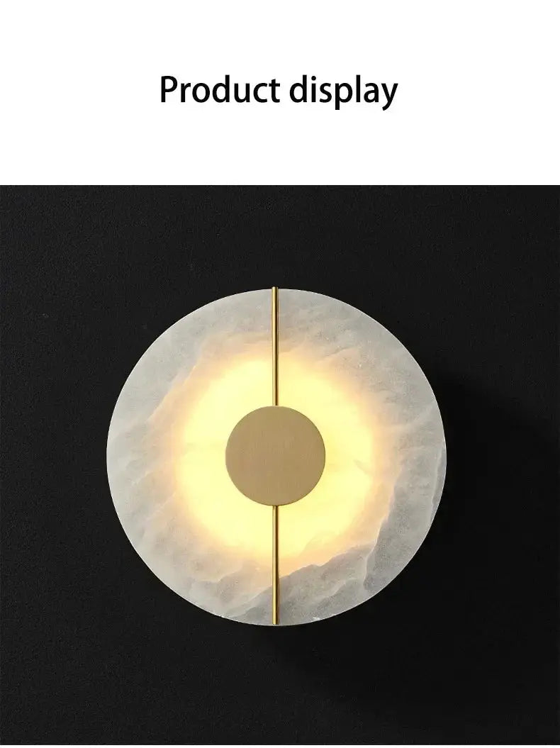 Alabaster marble wall sconce by Simples Market; round disk with gold vertical rod and warm glow.