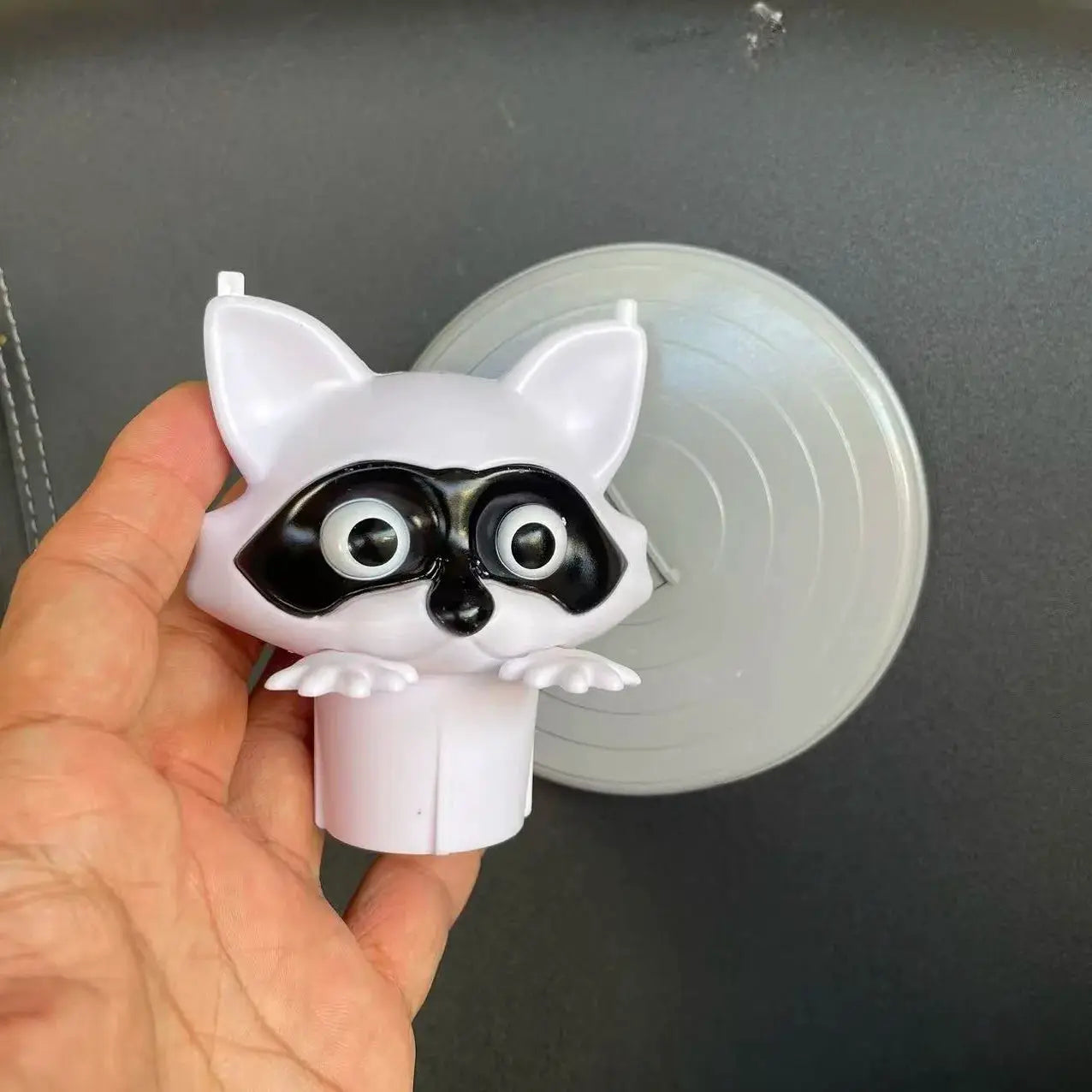 Toilet paper holder featuring a white cartoon raccoon figure with a black masked face and big eyes, bathroom decor.