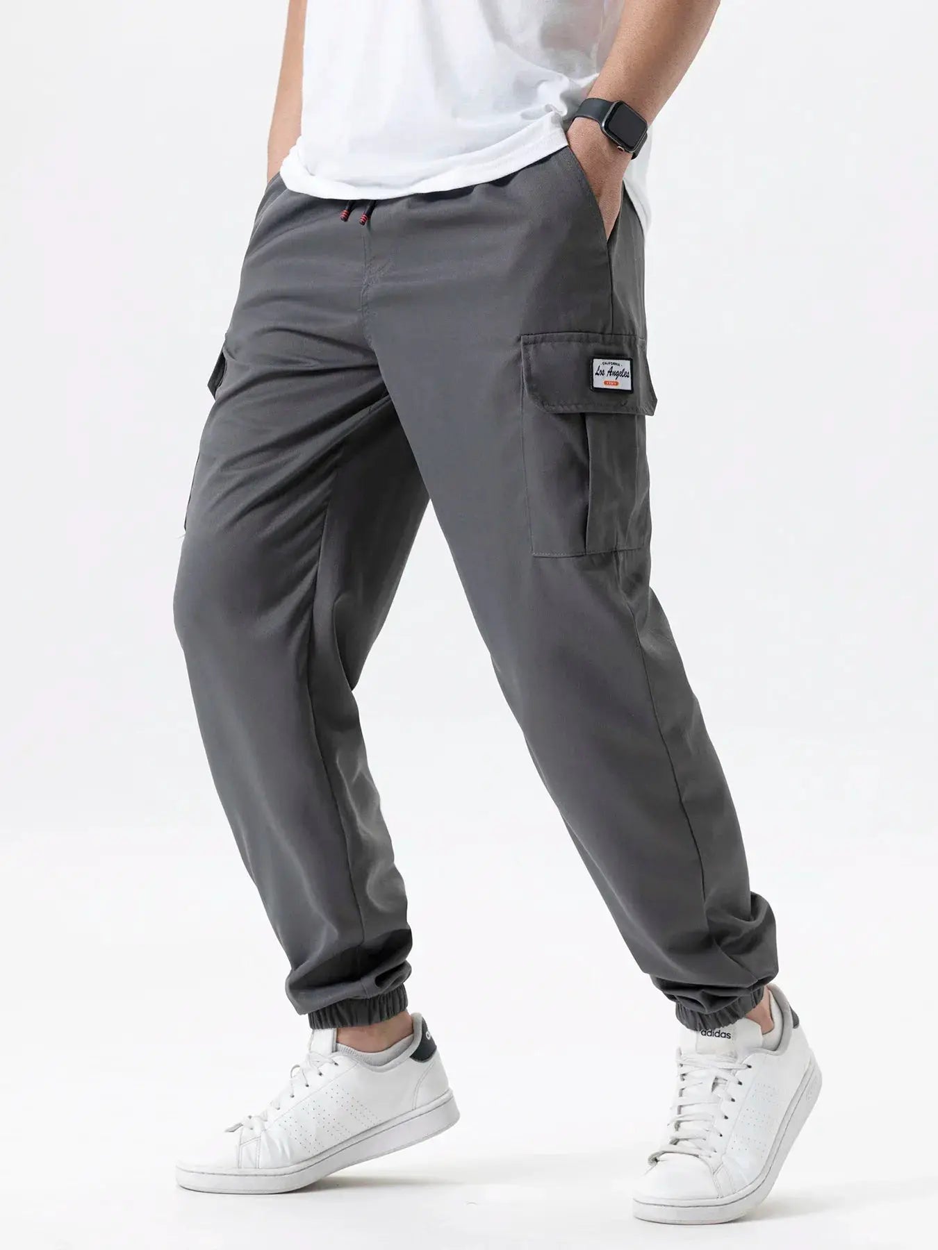Men's gray cargo sweatpants with drawstring waist and side cargo pocket, paired with white Adidas sneakers.