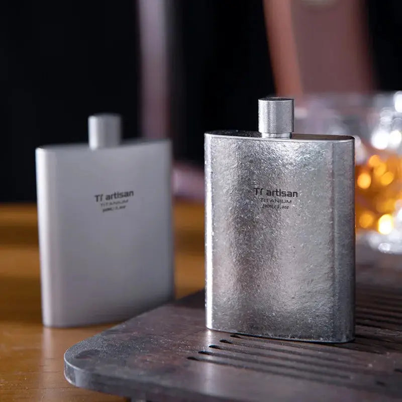 Tiartisan titanium hip flask 100ml by Simples Market, metallic silver finish with screw-cap, pair on wooden table.