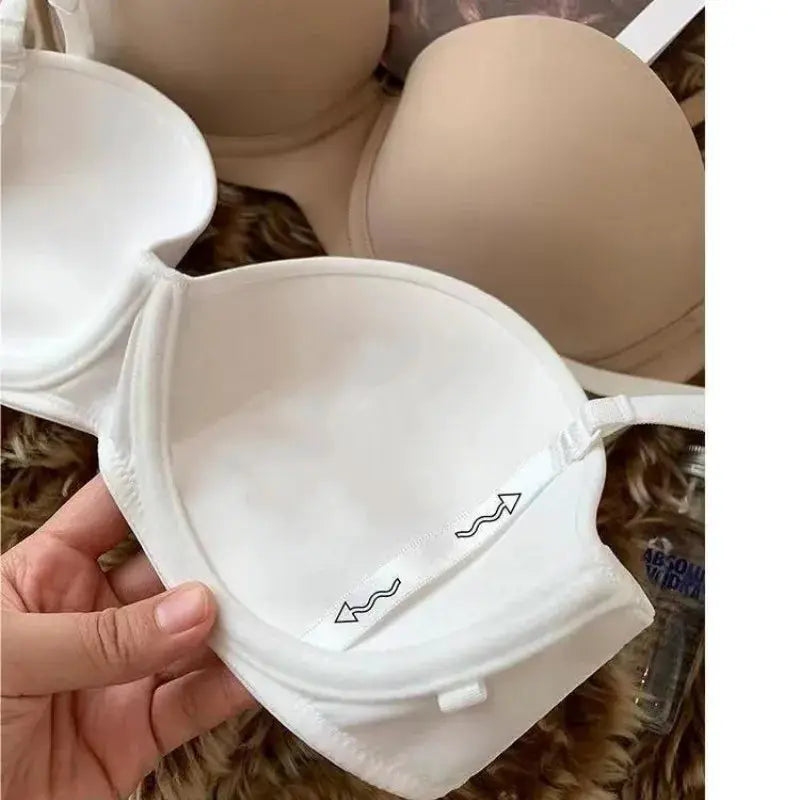 Two seamless bras in white and beige with back-hook closures; foreground white half-cup push-up style.