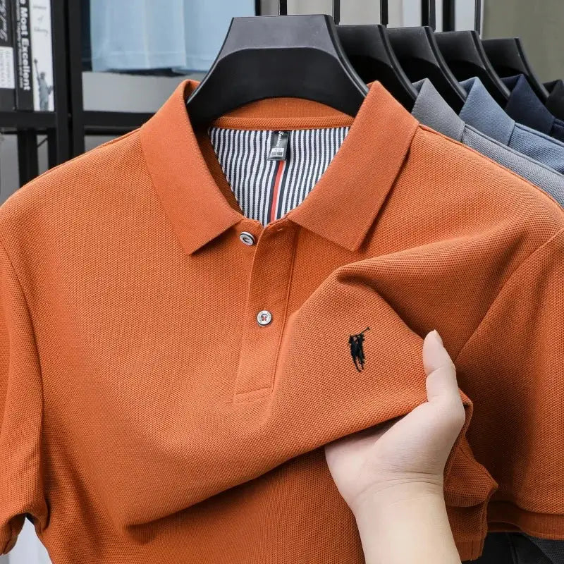 Orange cotton polo shirt with small black pony embroidery on chest, short sleeves; several polo shirts on display
