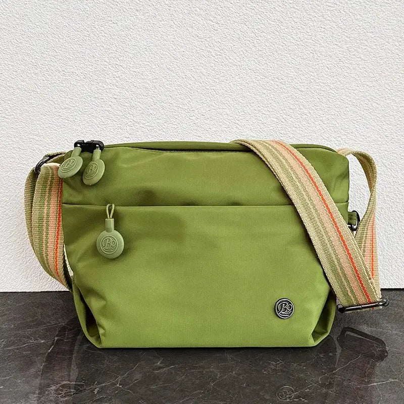 Ultra-light nylon crossbody bag for women by Simples Market, olive green with striped strap and zipper closure.