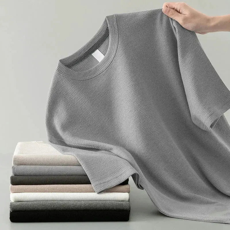 Korean-style men's waffle-knit short-sleeve T-shirt in gray, draped over a stack of assorted colors.