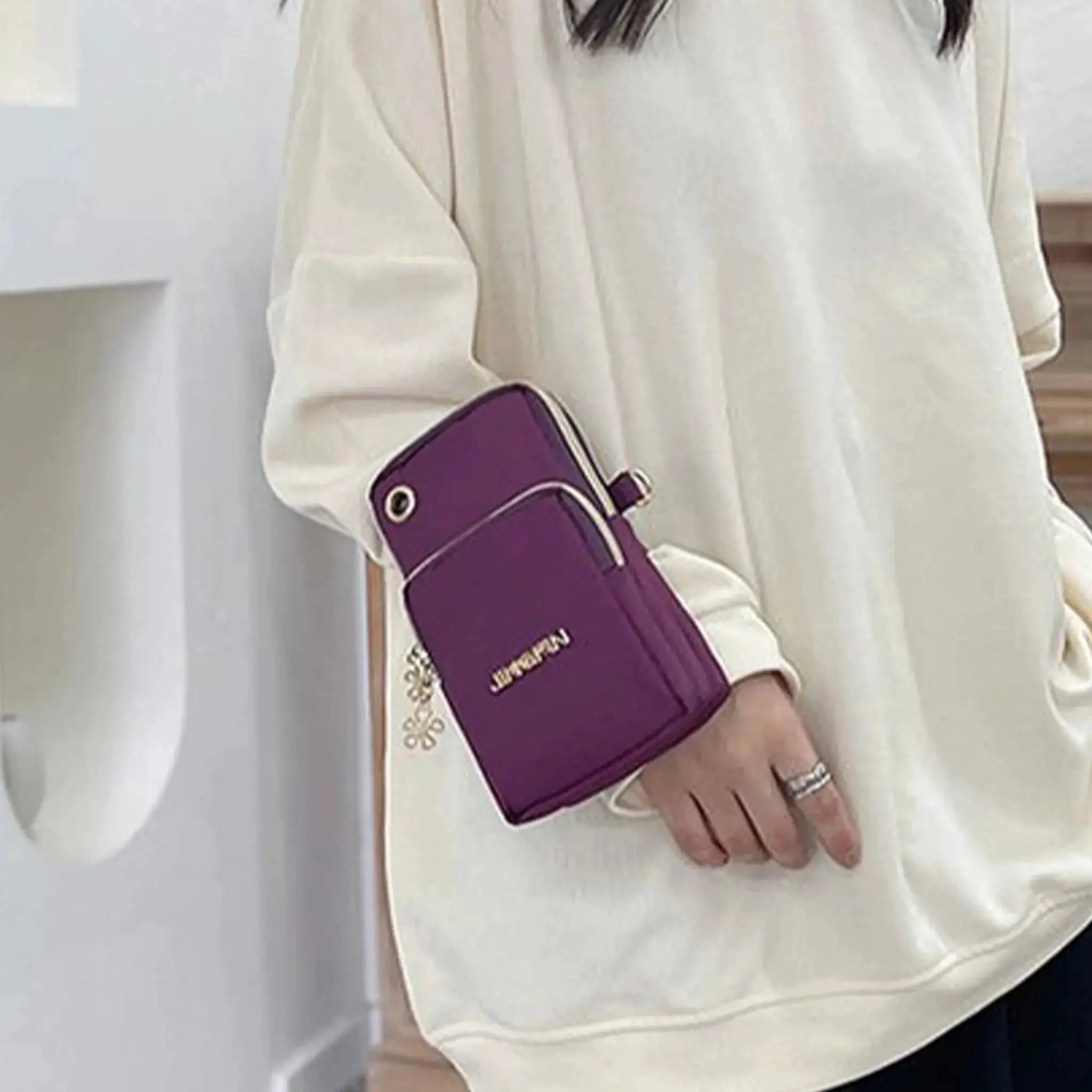 Mobile phone bag by Simples Market in purple, worn as a crossbody by a woman in a cream top.
