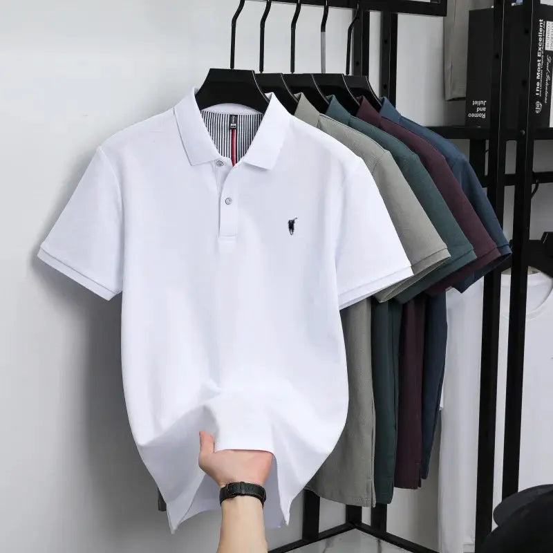 White 100% cotton short-sleeve polo shirt with small chest embroidery, displayed among assorted polo tops on a rack.