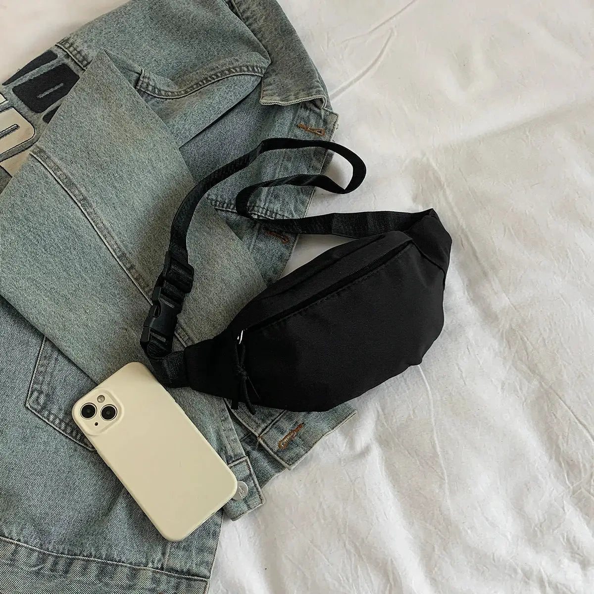 Fanny pack waist bag in black with adjustable strap, shown with a denim jacket and smartphone.