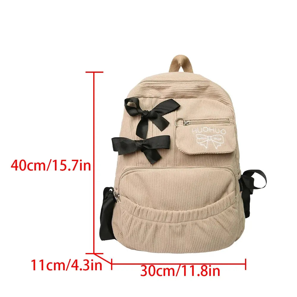 Simples Market beige corduroy backpack with black bows, front pocket, top handle, ideal for college commuting.
