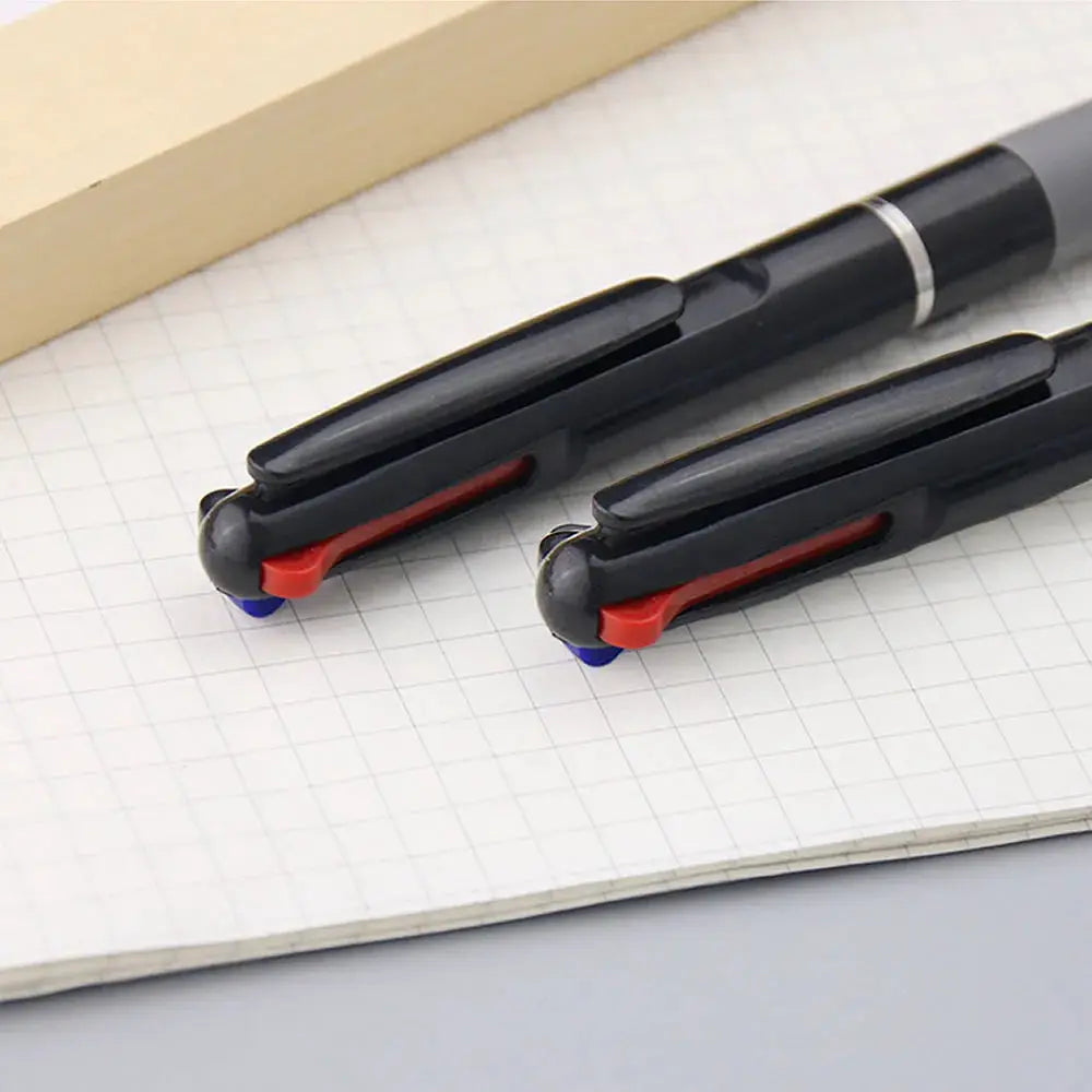 Two black 3-in-1 color ballpoint pens (red/blue/black) with red and blue selectors on grid notebook