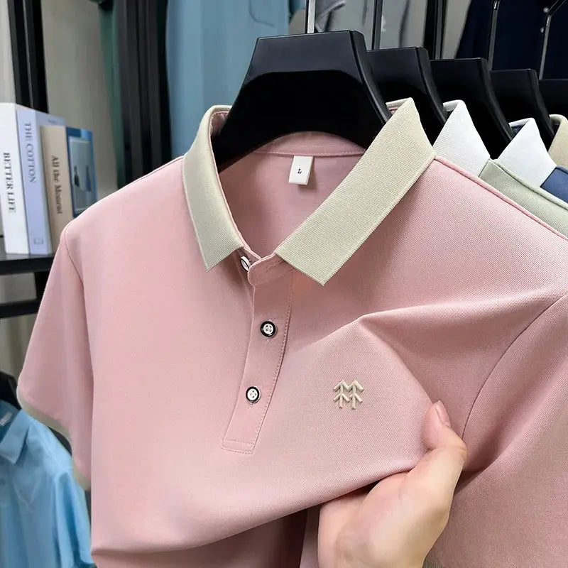 Pink polo shirt with cream collar; embroidered chest logo; on rack with 4 other shirts.